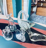 Photo showing the entire lot of five clear glass art pieces including four birds and one pear on a table surface.