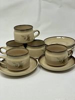 Full view of all cups stacked inside saucers showing the set of 6 cups and 6 saucers in beige-brown floral pattern.