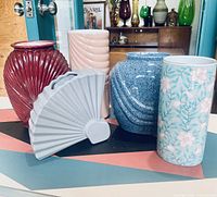 Five vintage ceramic vases placed on geometric patterned table showing all vases and their colors and texture details.