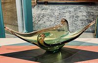 Full view of mid-century art glass dish with peach and green colors on black background, showing its flowing organic shape and curled ends.