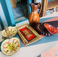 Lot of four mid century pottery pieces shown from front angle on tabletop including pitcher, relief server, cornucopia, and ashtray
