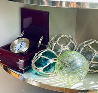 Five piece nautical lot displayed, showing four glass ball floats and one boxed nautical clock.