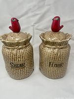 Pair of burlap textured ceramic canisters labeled Sugar and Flour with red cardinal bird figurines on lids.
