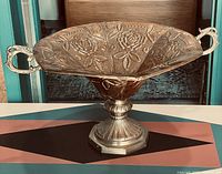 Full view of vintage copper and brass floral pedestal dish on hexagonal base with two handles and raised floral decoration on bowl.