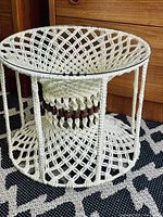 Full view of the handmade macrame side table showing the rope latticework, wood bead detailing, and glass top on a patterned rug.