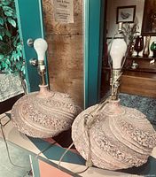 Pair of round terracotta clay lamps with textured floral patterns on a table, one lamp socket missing some parts
