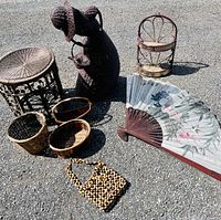 Multiple dark toned wicker items including baskets, plant stand, decorative lady figure, stool or side table, and folding fan with floral design, plus a beaded handbag