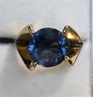 Top view of ring showing round blue faceted stone in four-prong setting and gold plated shoulders