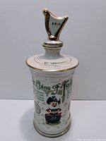 Front view of the white ceramic decanter with colorful Irish illustrations and gold accents, stopper labeled 'ERIN'.