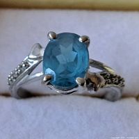 Close-up photo of sterling silver ring with oval blue topaz gemstone and decorative band detailing.
