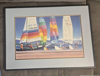 Framed print showing colorful sailboats with bright sails, matted with white border and framed in dark frame.