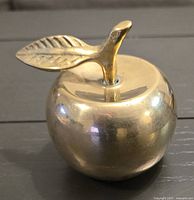 Front view of brass bell shaped like an apple with leaf handle showing polished surface and shape detail.