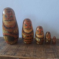 Five cat nesting dolls arranged in descending order of size on a wooden surface.