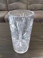 Photo of a thick, heavy crystal vase with intricate cut glass designs placed on a dark wooden surface with a couch in the background.