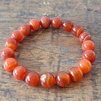 Fire agate beaded stretch bracelet laid flat on a wooden surface, showing the round polished beads with natural banding patterns.