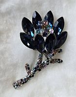 Front view of a silver-tone floral brooch with dark blue marquise rhinestones and multicolor small rhinestones on the stem and center