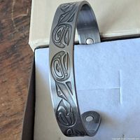 Front and side view of silver-toned metal cuff bracelet with raised and incised Haida salmon design