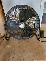 Front view of Honeywell fan showing the black metal cage, black three-blade fan, central Honeywell logo, and control box with speed knob set to off.