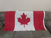New large Canada flag draped over a couch, showing full design with red maple leaf and red side bands.