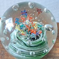 Front view showing colorful inner abstract floral shapes with air bubbles inside large glass paperweight.