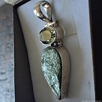 Front angled view of large sterling silver pendant showing faceted green topaz stone and rough large green stone below.