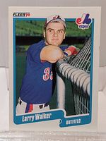 Front view of 1990 Fleer Larry Walker rookie baseball card showing Larry in Montreal Expos uniform leaning on a chain-link fence, with card details and logos visible.