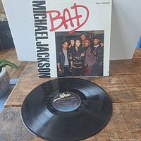 Vinyl record lying flat showing Epic label and front sleeve with 'BAD' and Michael Jackson text and photo of Michael Jackson with dancers.