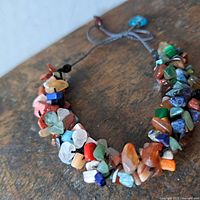 Close-up of multi-colored irregular gemstone chips strung on a grey adjustable pull string bracelet.