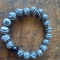 Close-up image of a stretch bracelet featuring round beads with black and white swirling patterns, placed on a wooden surface.
