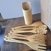 Bamboo kitchen utensils and cylindrical bamboo holder placed on wooden surface.