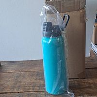 Water bottle in plastic packaging next to a cardboard box on a wooden surface.