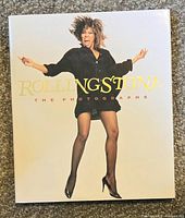 Cover of the photo book showing a woman jumping, wearing a black dress and heels with the title text 'ROLLING STONE THE PHOTOGRAPHS'.