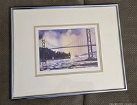 Photo showing the framed print with a simple silver frame and double matting; the artwork depicts a scenic view of the Lions Gate Bridge over water under purple sky.