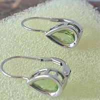 Pair of sterling silver earrings with green pear-shaped gemstones on a light foam background.