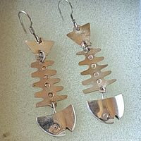 Pair of sterling silver earrings laid flat on a pale textured surface, showing the fish bone design elements.