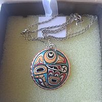 Photo showing sterling silver necklace with round Indigenous-style pendant inside a display box with light green padding.