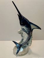 Full view of ceramic marlin-shaped decanter showing detailed fish figure and ocean wave base, 15.5 inches tall.
