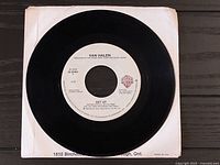 Black 7-inch vinyl record labeled "Get Up" by Van Halen with white label and Warner Bros. logo, placed on a black surface with a white paper sleeve beneath.