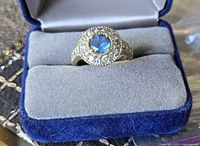 Front view of the vintage costume ring in blue box showing large blue center stone surrounded by small clear stones.