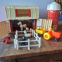 Overall view of all components of the Fisher-Price barn playset laid out on table including barn, silo, tractor with farmer and clown, animal figures, and fencing panels.