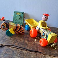 Photo showing Happy Hauler pull tractor with yellow trailer and toy driver, pull-along bug toy, and green toy radio.