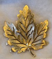 Front view of the gold-tone maple leaf brooch showing detailed veining and lobed leaf shape.