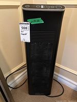 Full view of tall black Ionic Pro Platinum air cleaner positioned against a wall, showing front grill and power cord, with label indicating dimensions 8x7x26 inches.