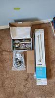 View of Aqua Care shower head with hose, boxed, along with Moen 24 inch double towel bars in original packaging and an additional small boxed item