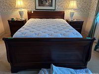 Full frontal view of the sleigh bed showing detailed wood veneer footboard, mattress surface, and flanking nightstands with lamps.