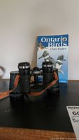 Carl Wetzlar binoculars in front of the Ontario Birds book, showing front and side details, tagged for identification and verification of lot contents.