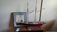 Bluenose 1921 detailed wooden model ship with two masts, rigging lines, and mounted on wooden base with framed boat print behind it.