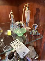Shelf displayed glass perfume bottles and atomizers in various styles and colors.