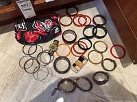 Photo showing multiple metal and plastic bracelets arranged on the floor with a black fabric bag with floral print.