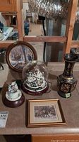 Overview of the lot with all items, including plates, framed prints, vase, and holiday decoration under glass dome